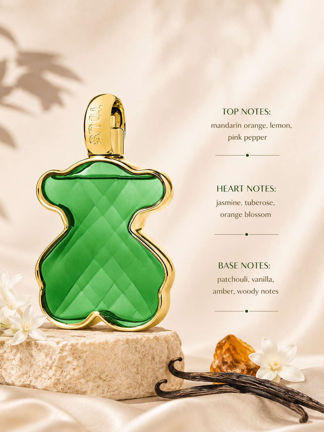 TOUS green bear-shaped perfume bottle with gold trim displayed on a stone pedestal, surrounded by vanilla pods, white blossoms, and amber resin, highlighting its citrus-floral fragrance notes.