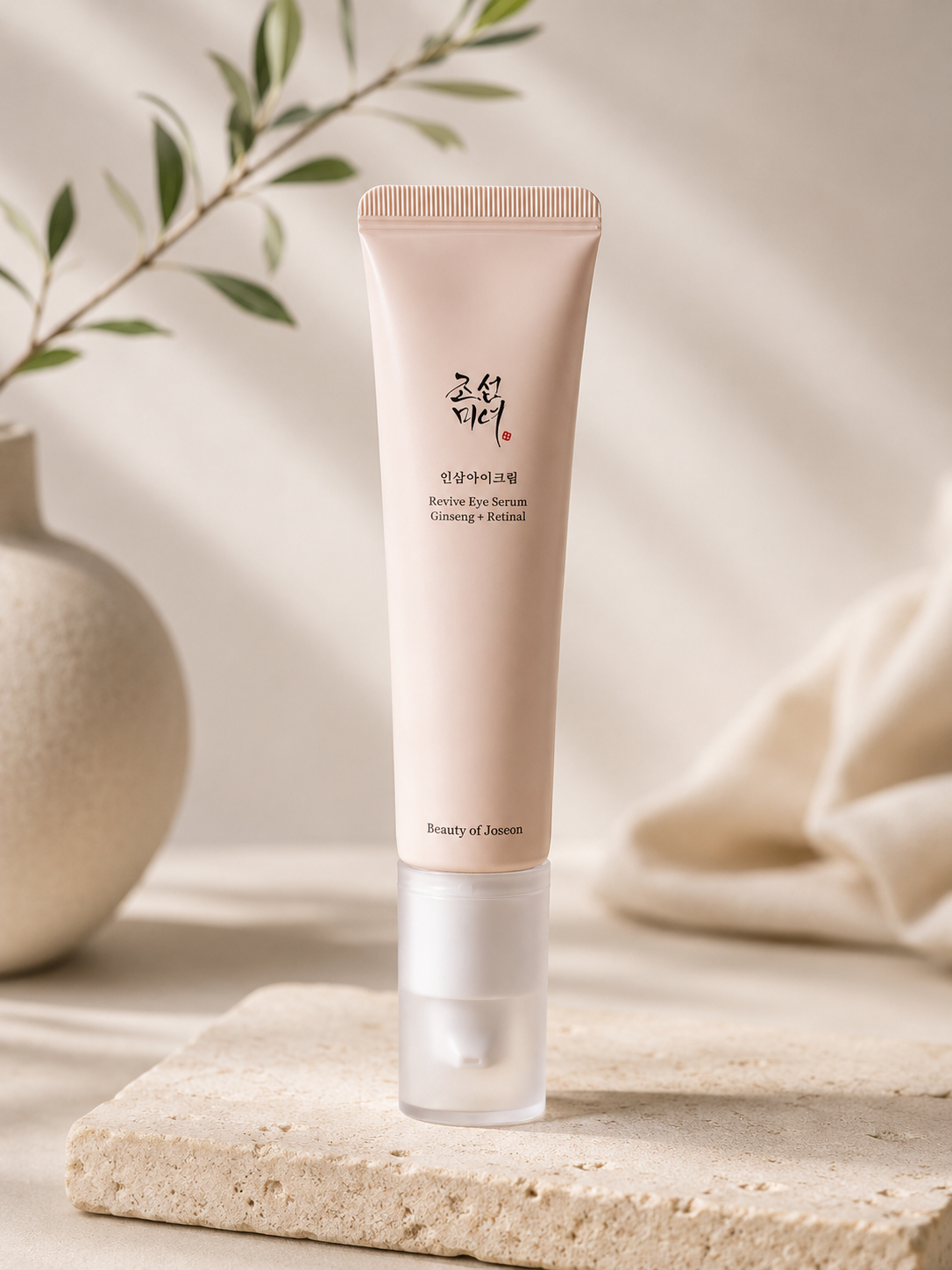Blush pink eye serum tube by Beauty of Joseon with clear pump, Korean script label, on stone slab with greenery and soft fabric background